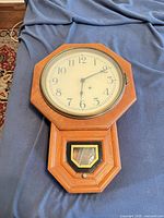 Front view of octagonal wood wall clock showing dial and lower door