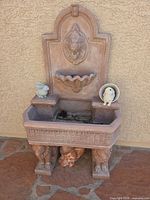 Full view of terracotta concrete wall fountain with decorative figurines placed on and beneath basin
