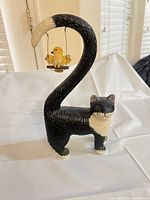 Full view of cat figurine with curved tail and bird swing