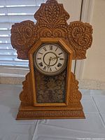 Front view of ornate carved oak mantel clock with glass door and Roman numeral dial