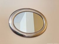Full view of oval silver metal mirror on wall