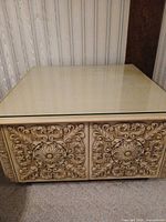 Full view of square ivory coffee table showing carved front and glass top