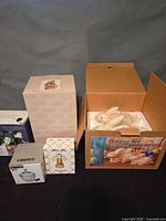 All boxed items: bunny set box open showing two cream ceramic rabbits, LED garland box, Liberty candy dish box, crystal angel box