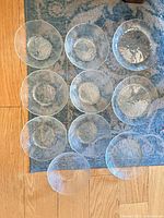 Overhead view of ten clear ribbed pressed glass plates laid out on rug
