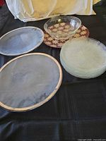Group view of all charger plates, bowl and stack of dinner plates on black surface