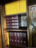 Shelf with loose yellow-border magazines above two rows of maroon hardbound volumes