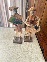 Front view of both papier-mâché fisherman figurines with accessories and bases visible