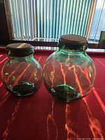 Both green glass jars with corks standing side by side