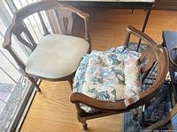 Two wooden dining armchairs with beige seats and one floral cushion