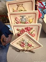 Four ceramic floral plaques displayed on tabletop stand