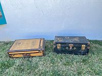 Closed tan and black steamer trunks on grass