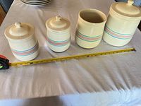 Four striped ceramic canisters on table with tape measure