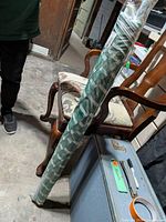 Full view of rolled, tagged beach umbrella leaned against chair with suitcase and partial view of woven box