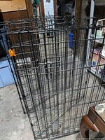Front view of folded black metal pet fence showing latch and orange clip