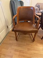 Front view of chair showing leather seat, backrest, armrests, turned legs