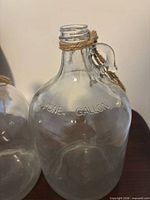 Close-up of first clear glass jug showing ONE GALLON embossing and twine