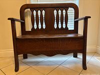 Front view of oak storage bench showing back splats, armrests and scalloped apron