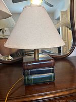 Small lamp with stacked-book base and cone shade on dresser