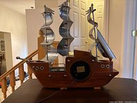Rear view of wooden sailboat clock showing metal sails, rear access panel, and power cord
