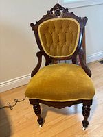 Front view of carved wood chair with tufted mustard velvet upholstery and front casters
