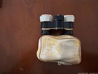 Binoculars resting on top of beige brocade zip case