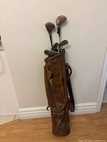 Full view of leather golf bag with clubs standing against wall