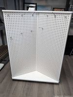 Front view of white triangular three-panel pegboard display with hooks