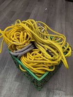 Heap of yellow braided rope and one grey rope segment inside green plastic crate on floor