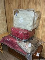 Stacked clear storage bags containing cream, red and beige comforters placed on wooden chest