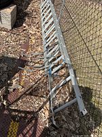 Full view of aluminum extension ladder with standoff attached, lying on ground