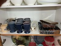 Cabinet shelf with full lot: blue mugs, GM mugs, stainless pitcher, corn dishes, utensil bin