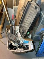 Plastic tote filled with assorted plumbing parts, black plastic drip pan on top