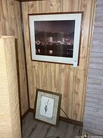 Corner view showing both framed prints: cityscape hung, botanical leaning