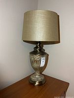 Full view of table lamp on wooden surface showing metal body and beige shade