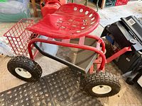 Side view of red rolling garden seat with basket, tray and tires