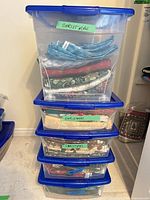 Stack of four clear bins with blue lids labelled "Christmas" containing folded fabrics