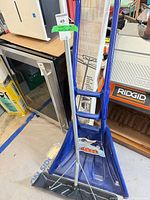 Blue plastic snow shovel standing with telescoping pole in background