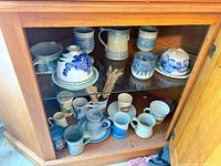 Cabinet view showing pitcher, two covered butter dishes, goblet, matching mugs and assorted mugs on lower shelf
