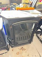 Front view of black Komodo electric stove fireplace heater showing arched glass door and decorative grate