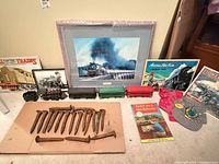 Group shot showing framed print, toy trains, posters, spikes, book, caps