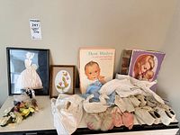 Overall lot showing framed artworks, books, baby clothing, shoes, corsages