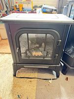Front view of black electric stove fireplace heater with glass door, logs visible
