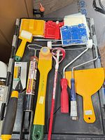Group on black lid: roller frames, trays, mixing paddle, trowels, caulk tube, plastic spreader