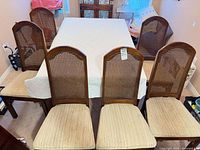 Six wood dining chairs around table showing cane backs and upholstered seats