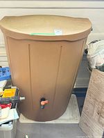 Front view of tan plastic rain barrel with lid and spigot