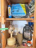 Shelf with Beacon hurricane lantern, felt-covered bottle, cream ceramic lamp base, orange flashlight visible foreground