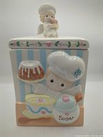 Front view of sugar canister showing raised design and lid figurine