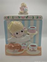 Front view of canister displaying relief artwork and lid figurine