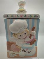 Front view of canister showing relief design and lid figurine