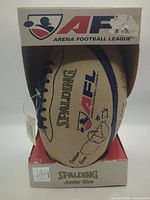 Front view of autographed Spalding AFL junior football in open-front retail box with hang tag
